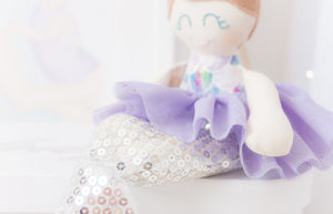 RubyBabyDesigns Keepsake Collective Mini Mee Ballerina Mermaid Heirloom Cloth Doll Decor, a scale printed body with lovely tones of lilacs, blues, aquas, greens, pinks, whites. Paired with a lilac tutu skirt and silver sequin mermaid tail. Ballerina bun sitting on top of her head in a wool blend toffee and a faux leather silver bow in her hair. Handmade and designed in Melbourne and environmentally friendly PET fill.